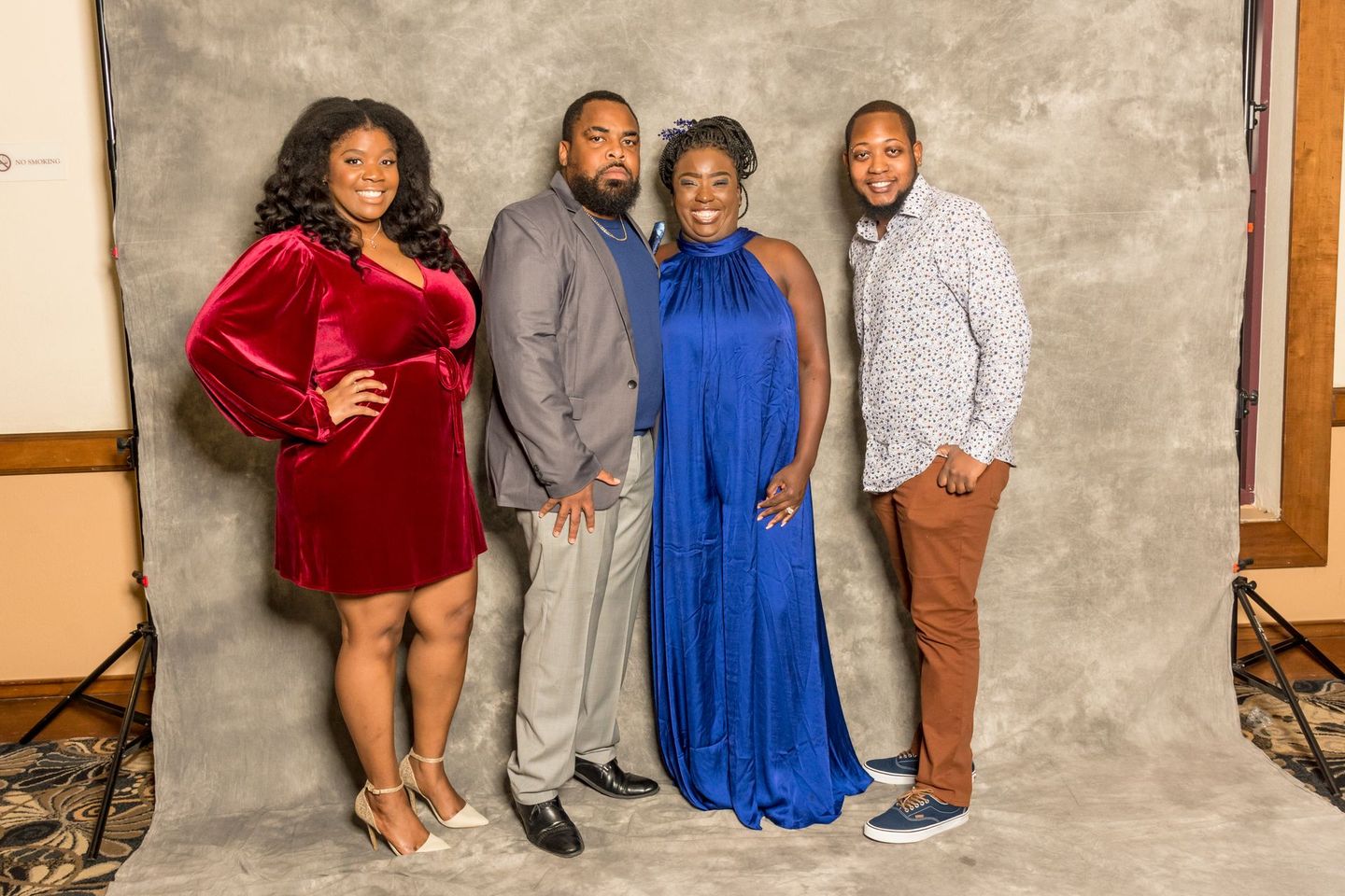 Four people posing in front of a gray studio backdrop, wearing colorful formal outfits.
