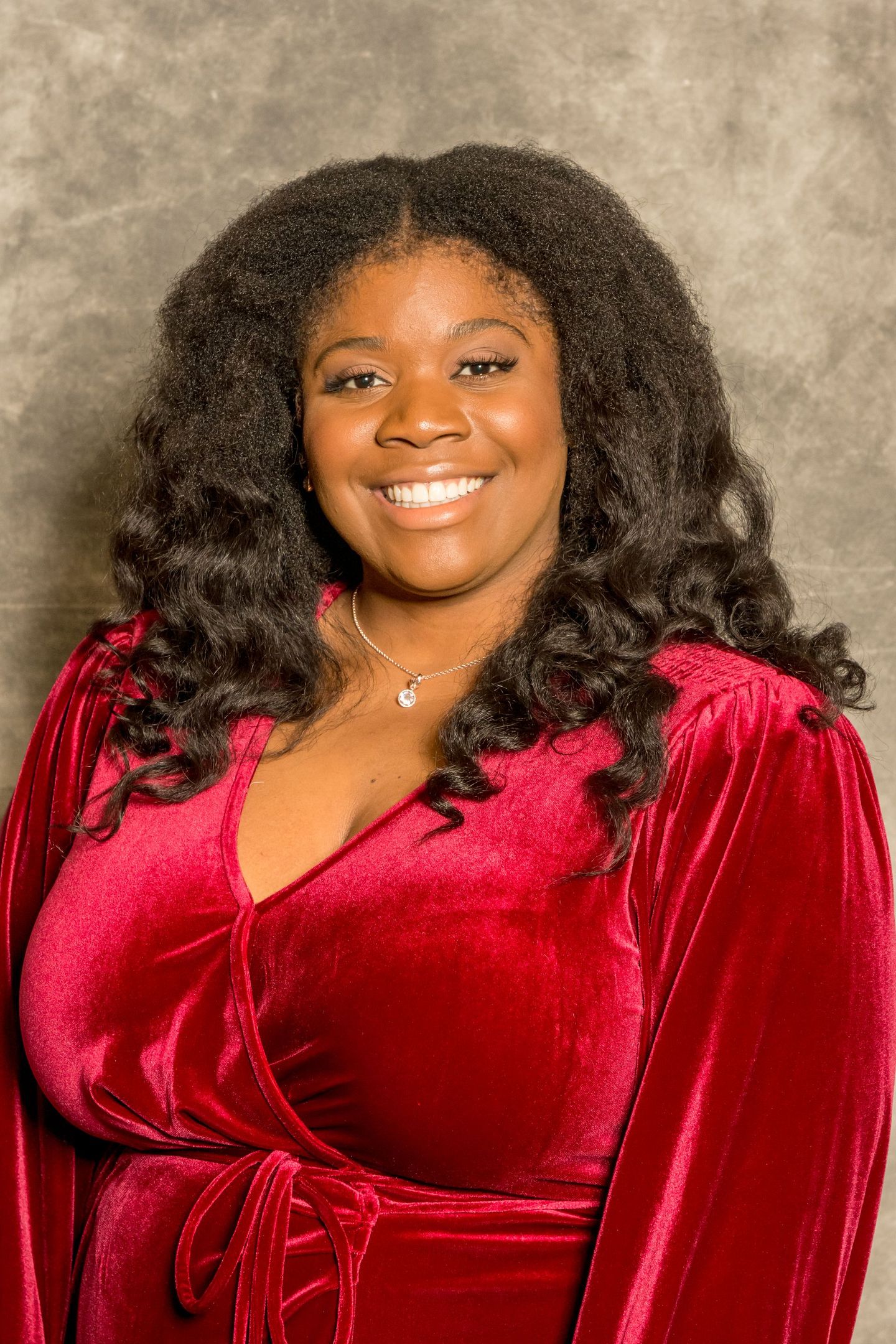 Woman smiling in a red velvet dress against a mottled studio backdrop