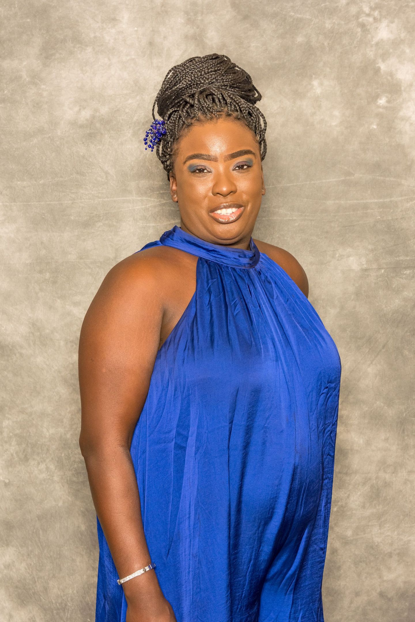 Woman in a royal blue halter dress, posing against a neutral textured backdrop.