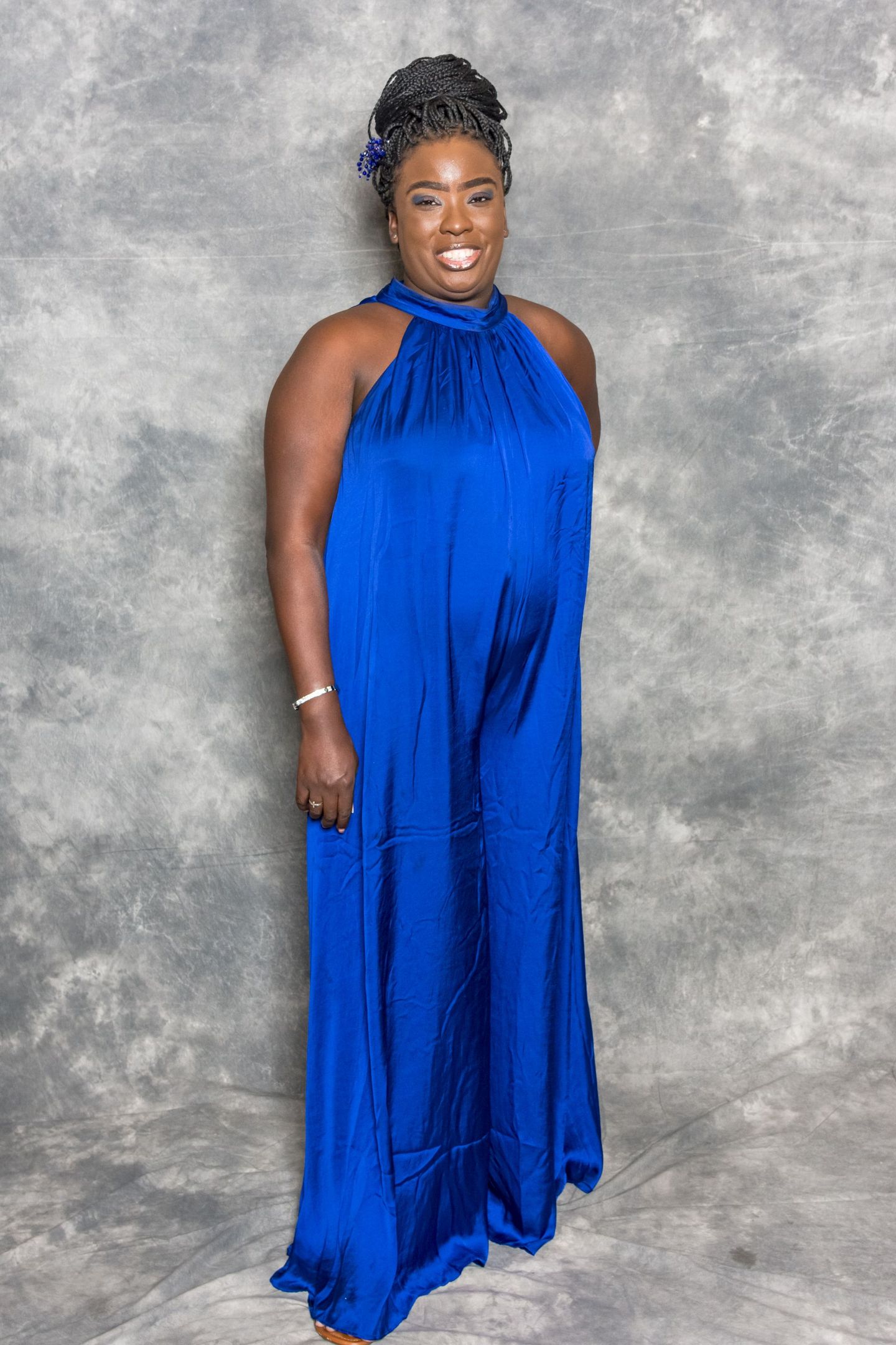 Woman in a bright blue halter gown standing and smiling against a gray backdrop