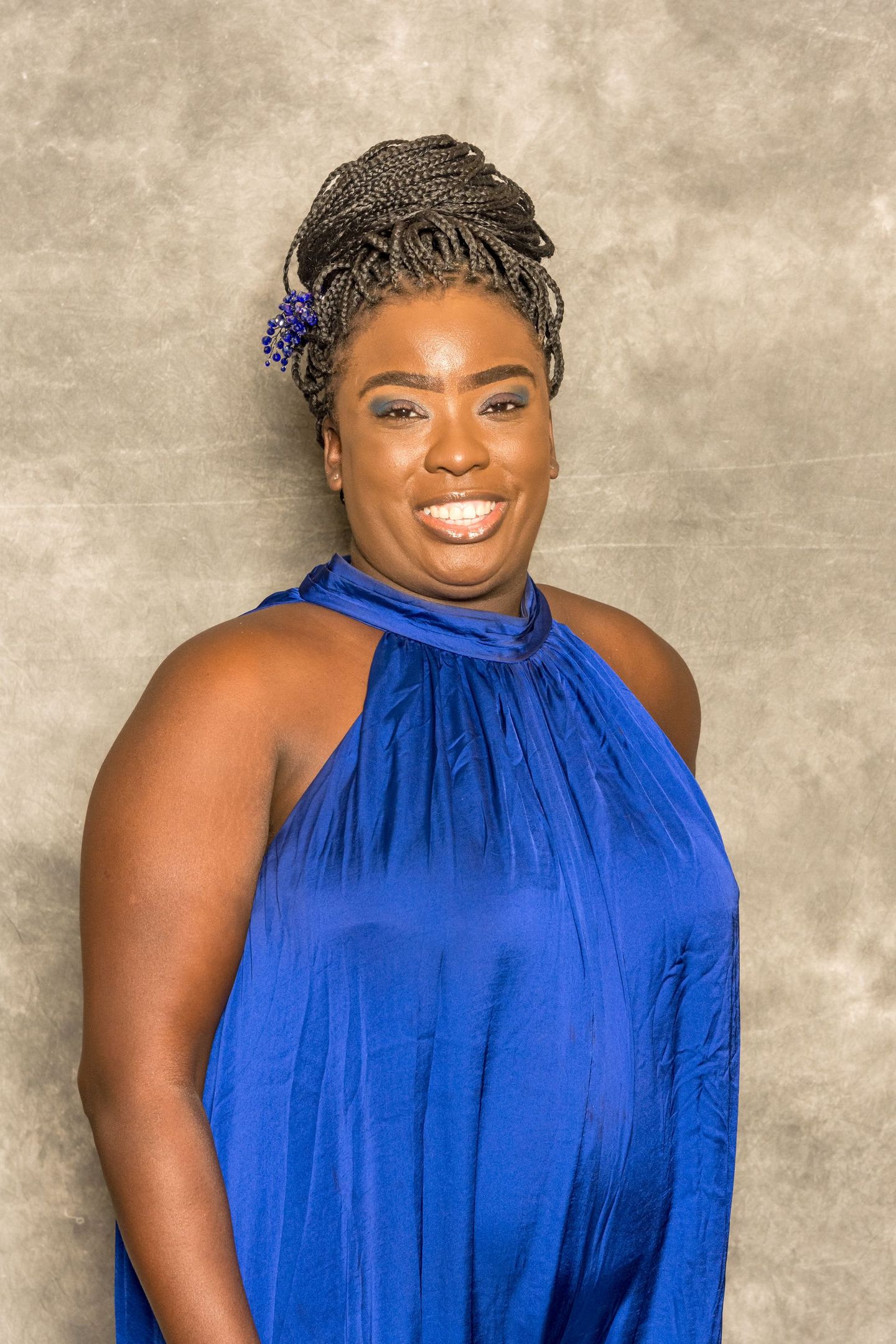 Woman in a blue halter dress, smiling against a neutral studio backdrop.