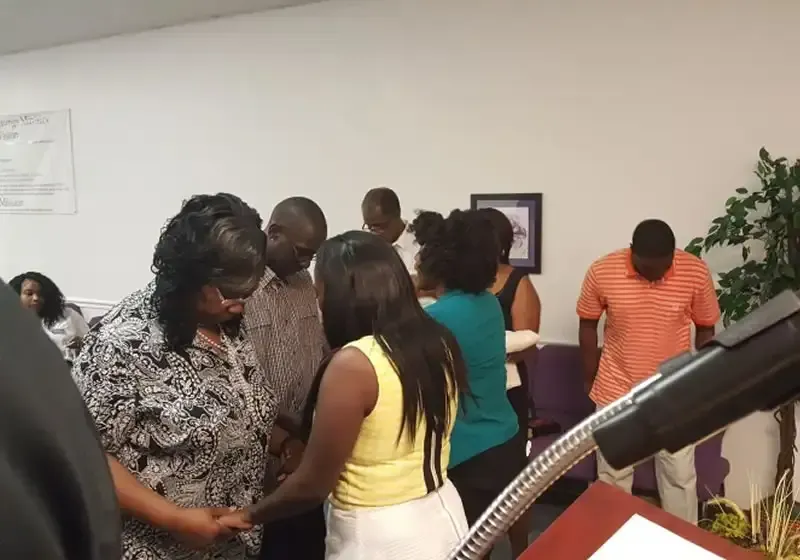 People gathered indoors near a podium, with one woman speaking and others standing in conversation.