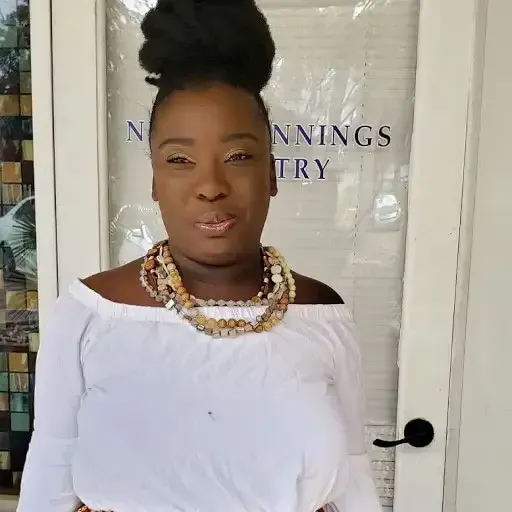 Woman in white off-shoulder top and layered necklace standing in front of a glass door