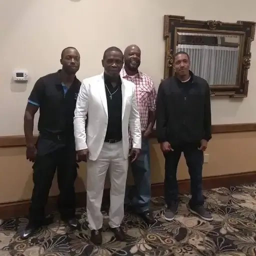 Four people posing indoors in front of a framed mirror, wearing dark and light casual outfits.