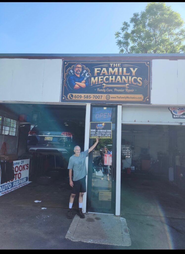Person standing at the entrance of Family Mechanics auto shop with cars inside and sign above.| The Family Mechanics - Cherry Hill