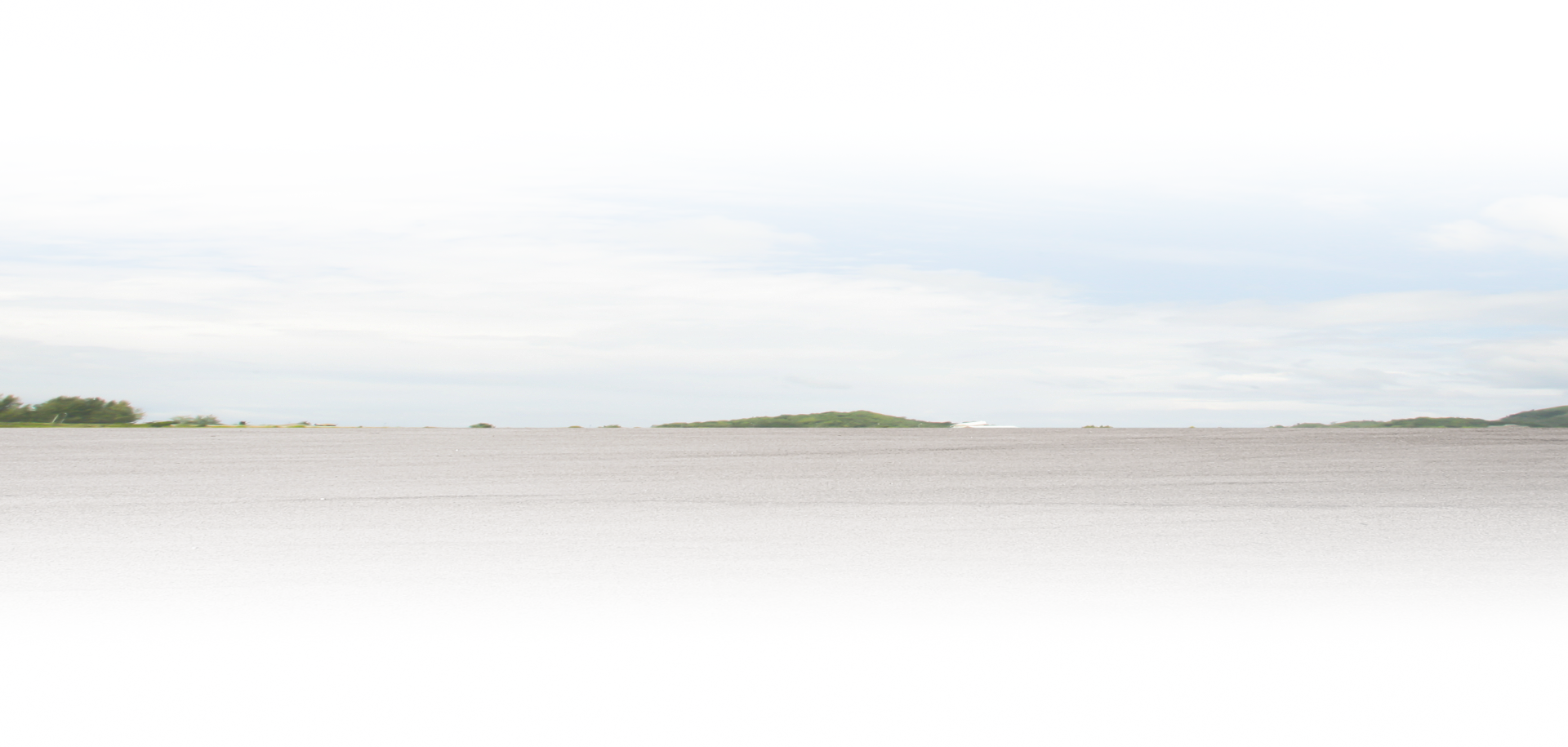 Bright sandy beach with calm water and a pale cloudy sky, distant land on the horizon | The Family Mechanics - Cherry Hill