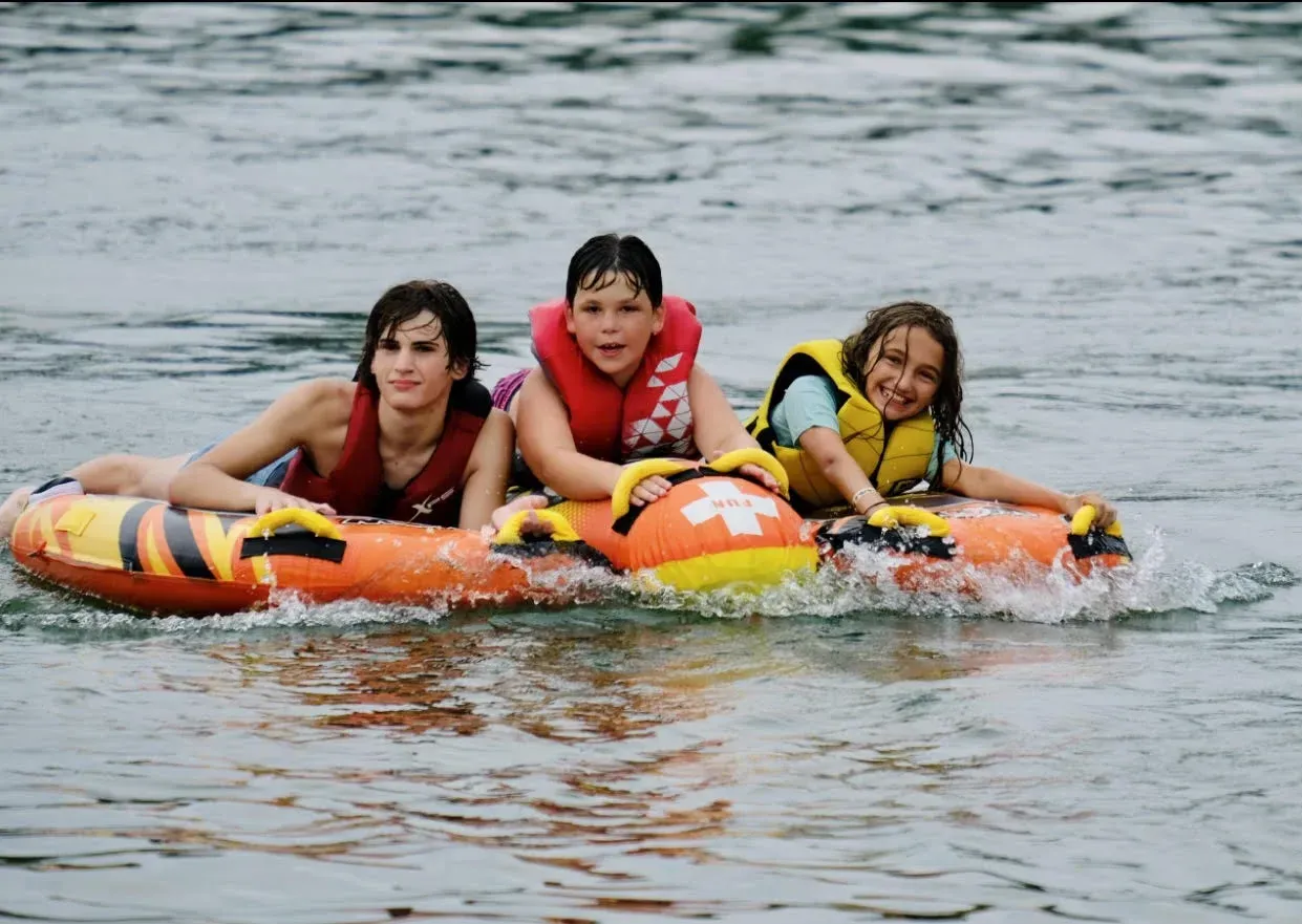 Three people on a tube, wearing life jackets, being pulled through water.