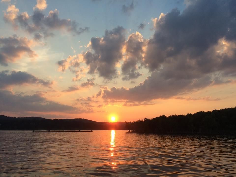 Sunset over lake with golden sunlight reflecting on the water, silhouetted shoreline.