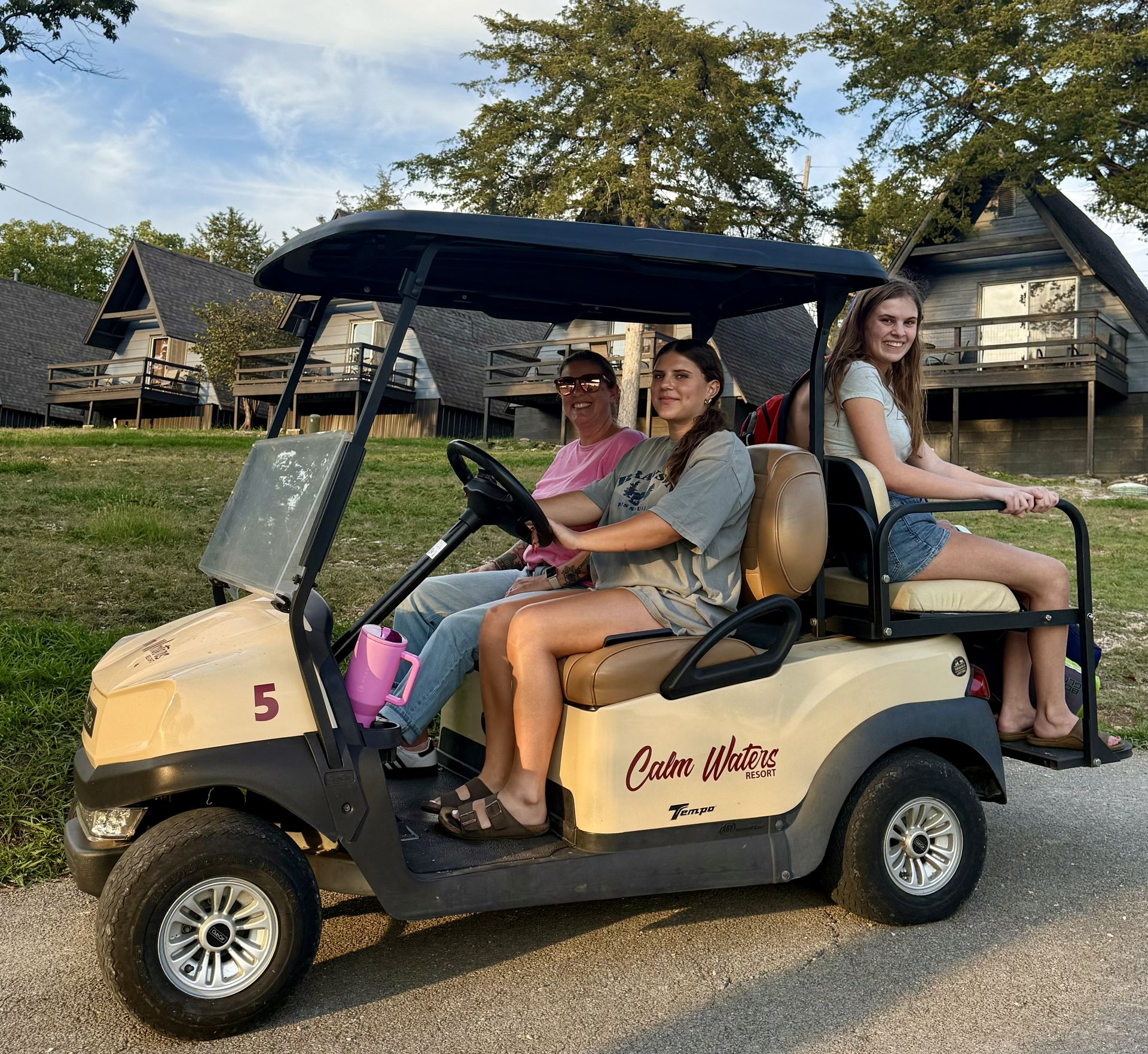 People riding in a white golf cart near wooden cabins. Some smiling.