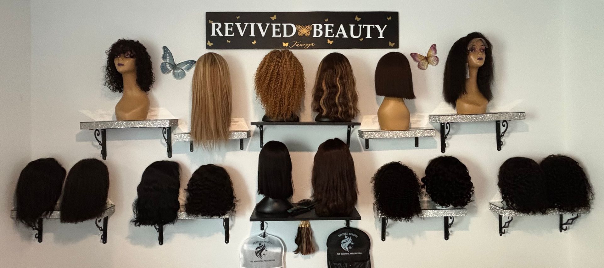 Wigs displayed on shelves with the sign Revived Beauty on a wall. Wigs displayed on shelves with the sign Revived Beauty on a wall.