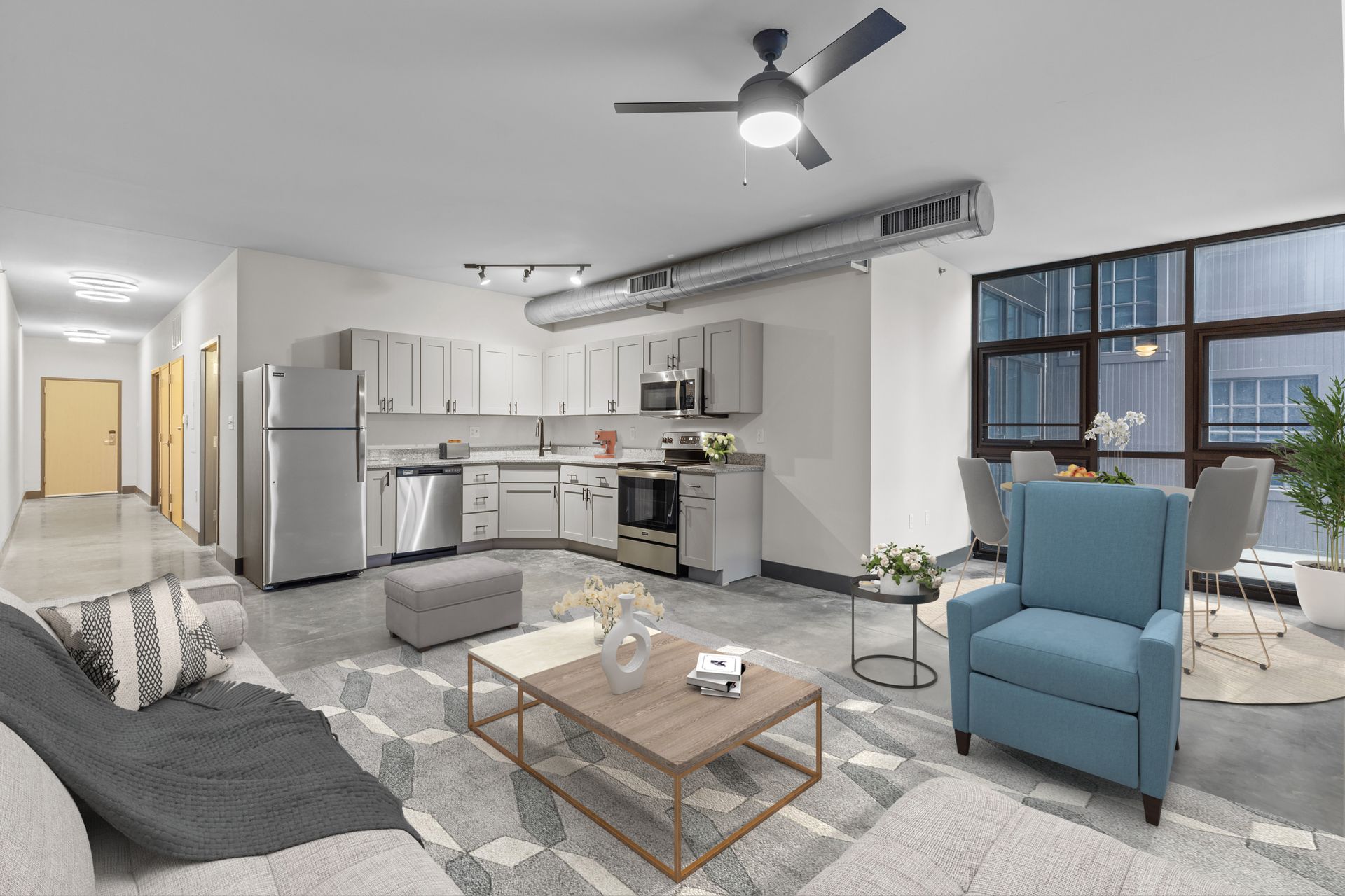 Bright modern apartment living room with gray sofa, blue chair, kitchen, and large window