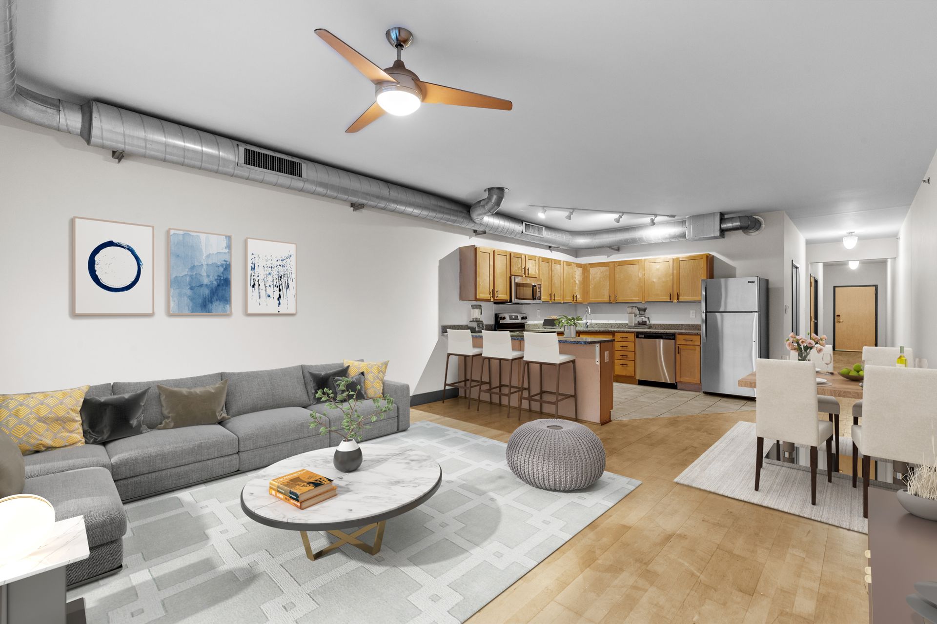 Open-concept living room with gray sofa, coffee table, dining area, and kitchen in the background.
