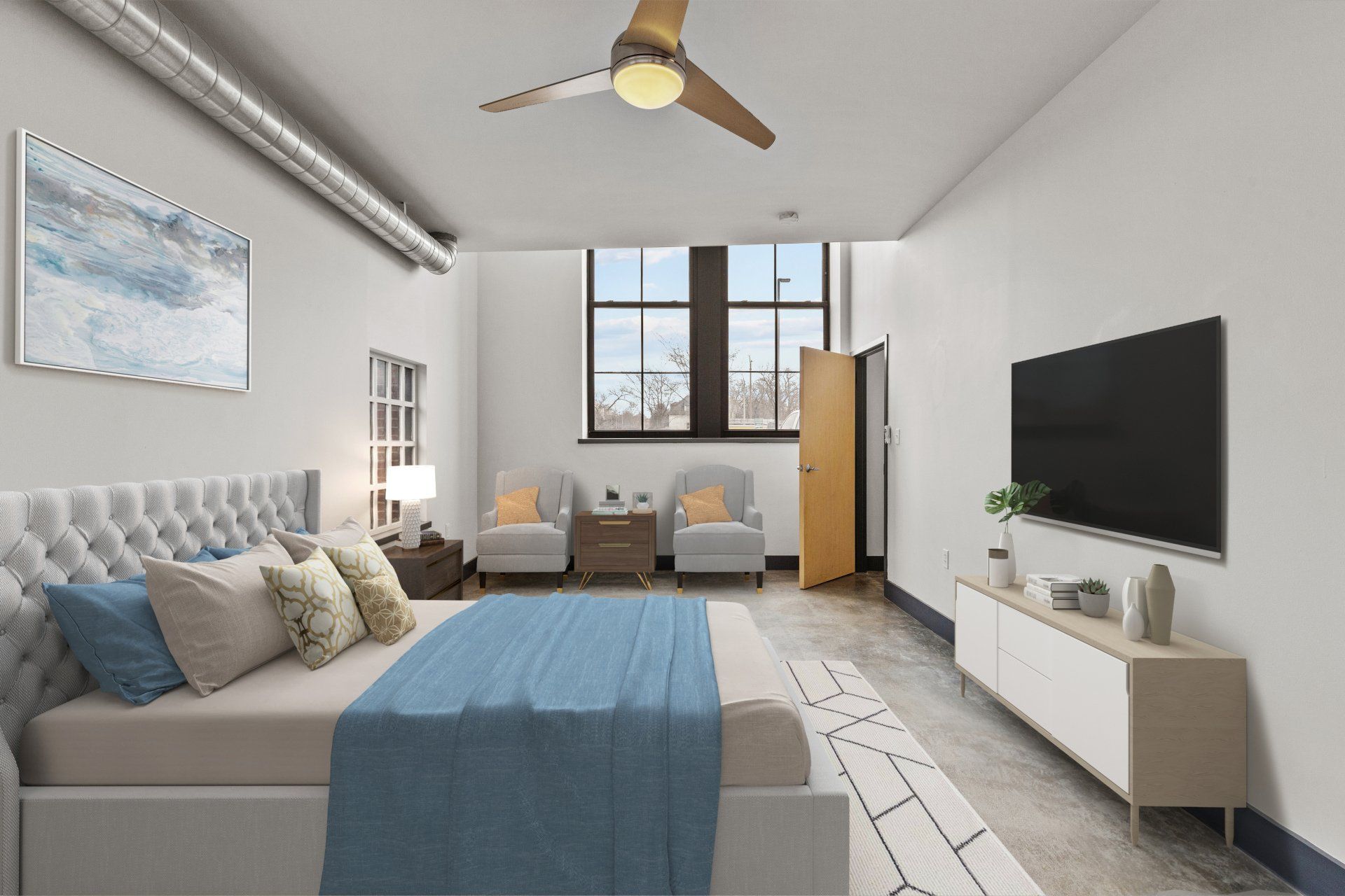 Modern bedroom with blue bedding, two chairs by the window, wall TV, and a ceiling fan