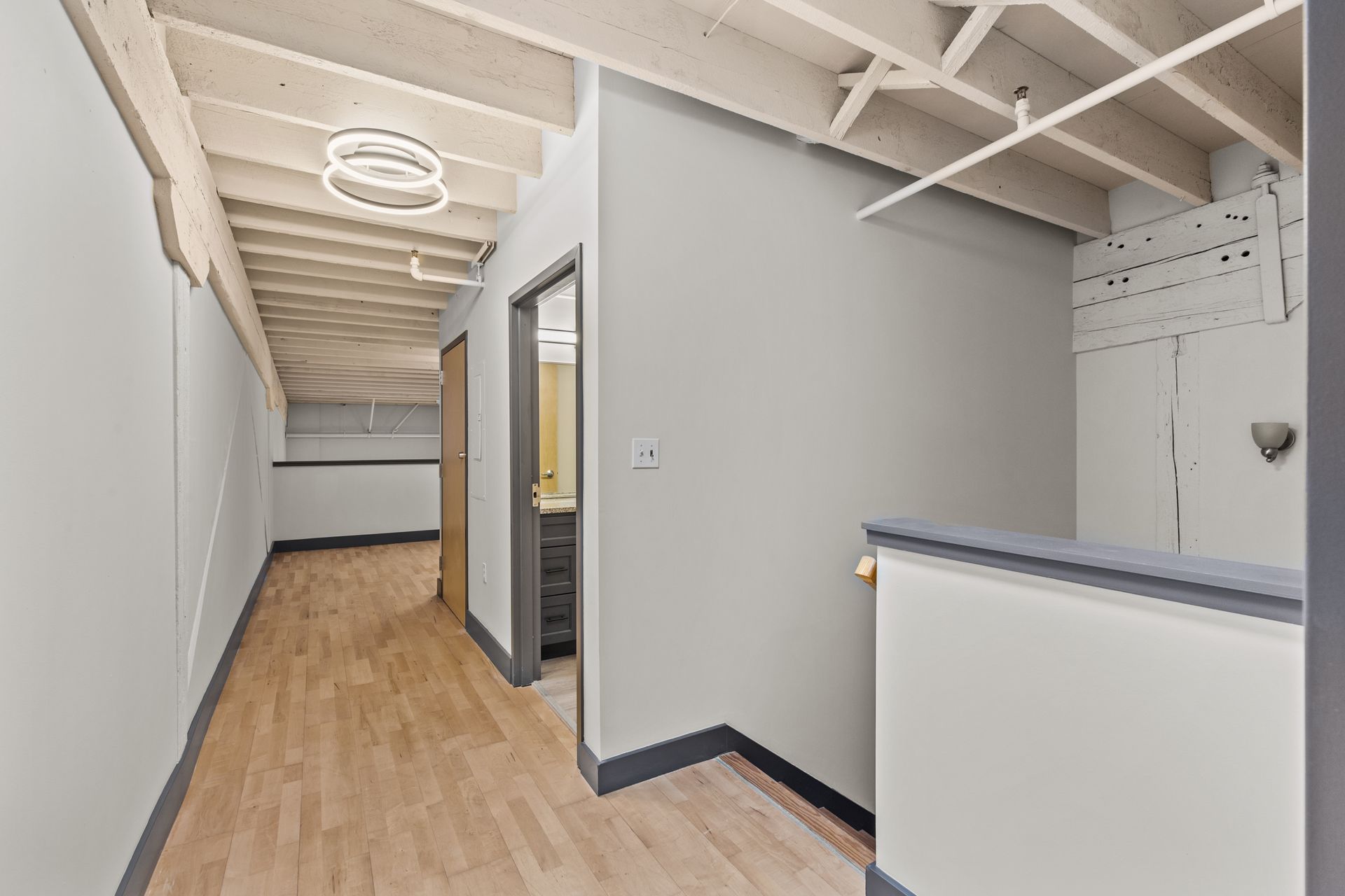 Narrow hallway with wood floor, gray walls, exposed ceiling beams, and a small utility nook.