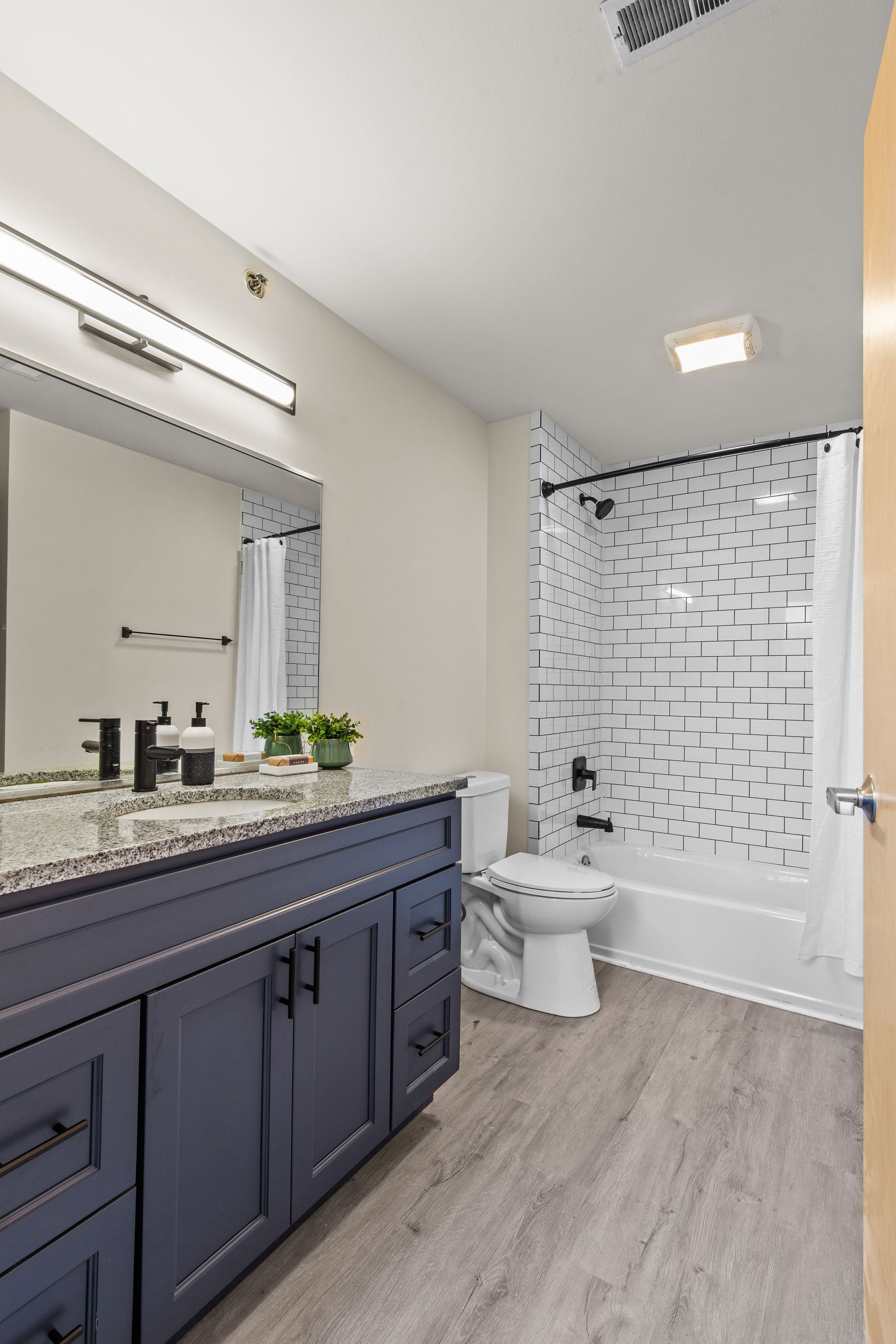 Modern bathroom with navy vanity, large mirror, toilet, and white shower curtain with black pattern