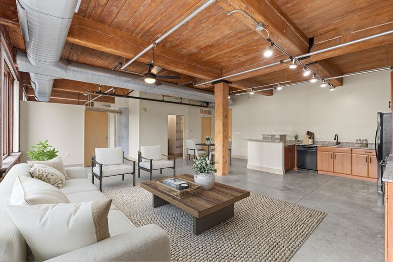 Open loft living room with exposed wood beams, white sofa, coffee table, and kitchen area