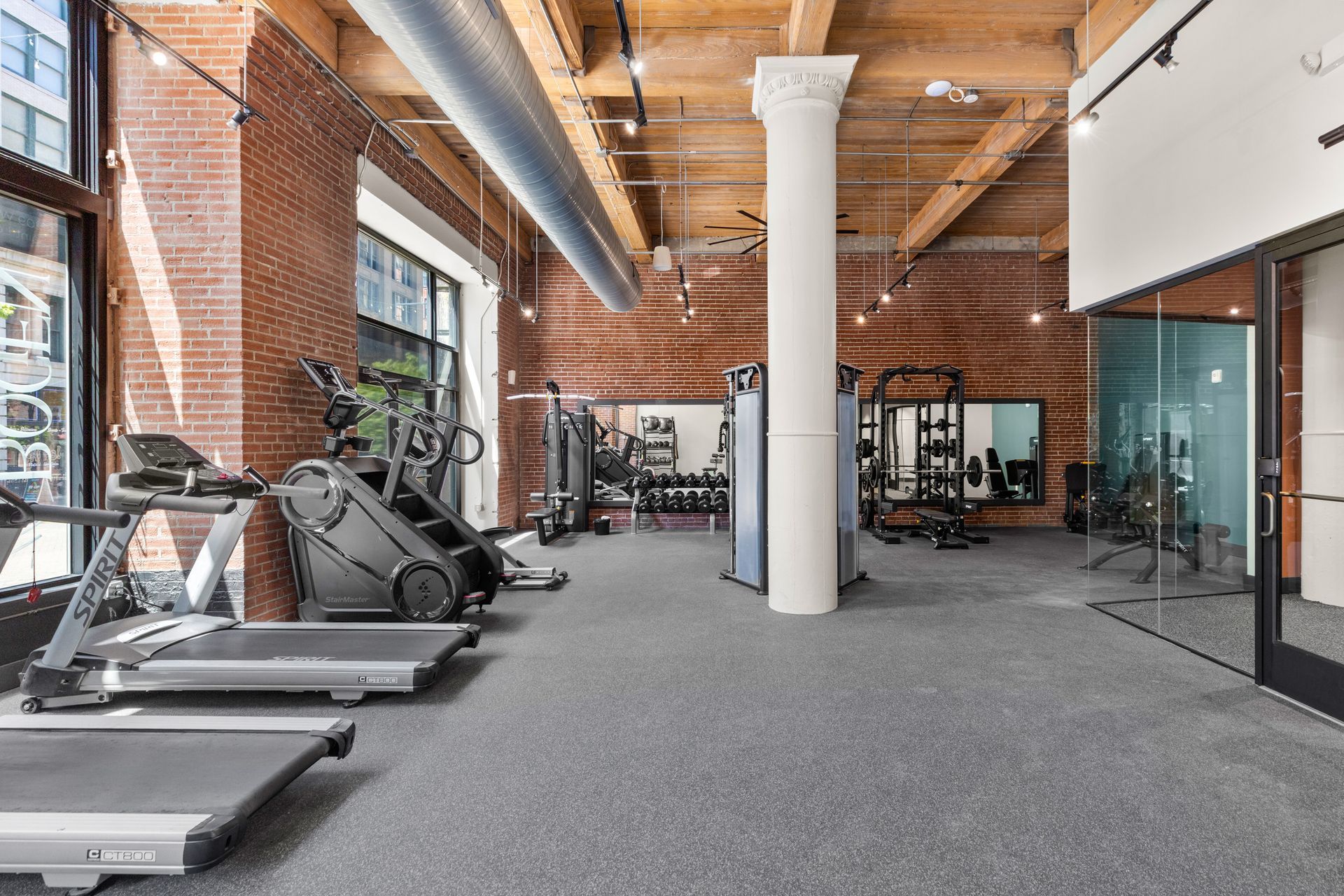 Modern gym interior with treadmills, exercise bikes, brick walls, and exposed wood ceiling