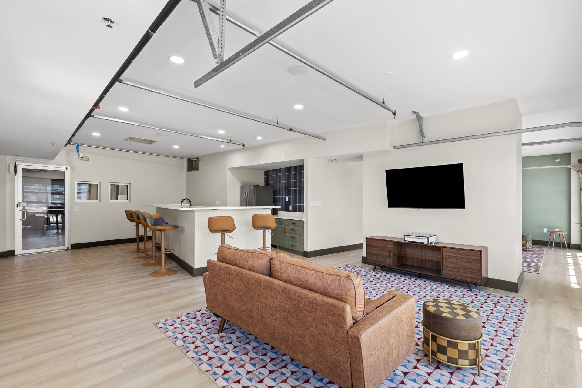 Bright modern living room with brown sofa, wall-mounted TV, kitchen island, and hardwood floors.