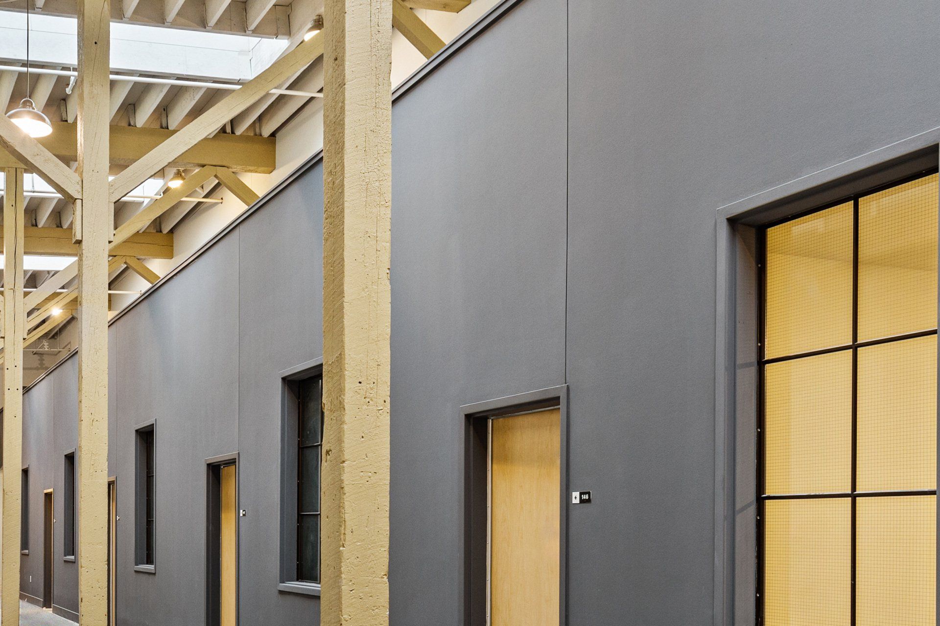 Modern office corridor with dark gray walls, wood doors, and exposed timber beams