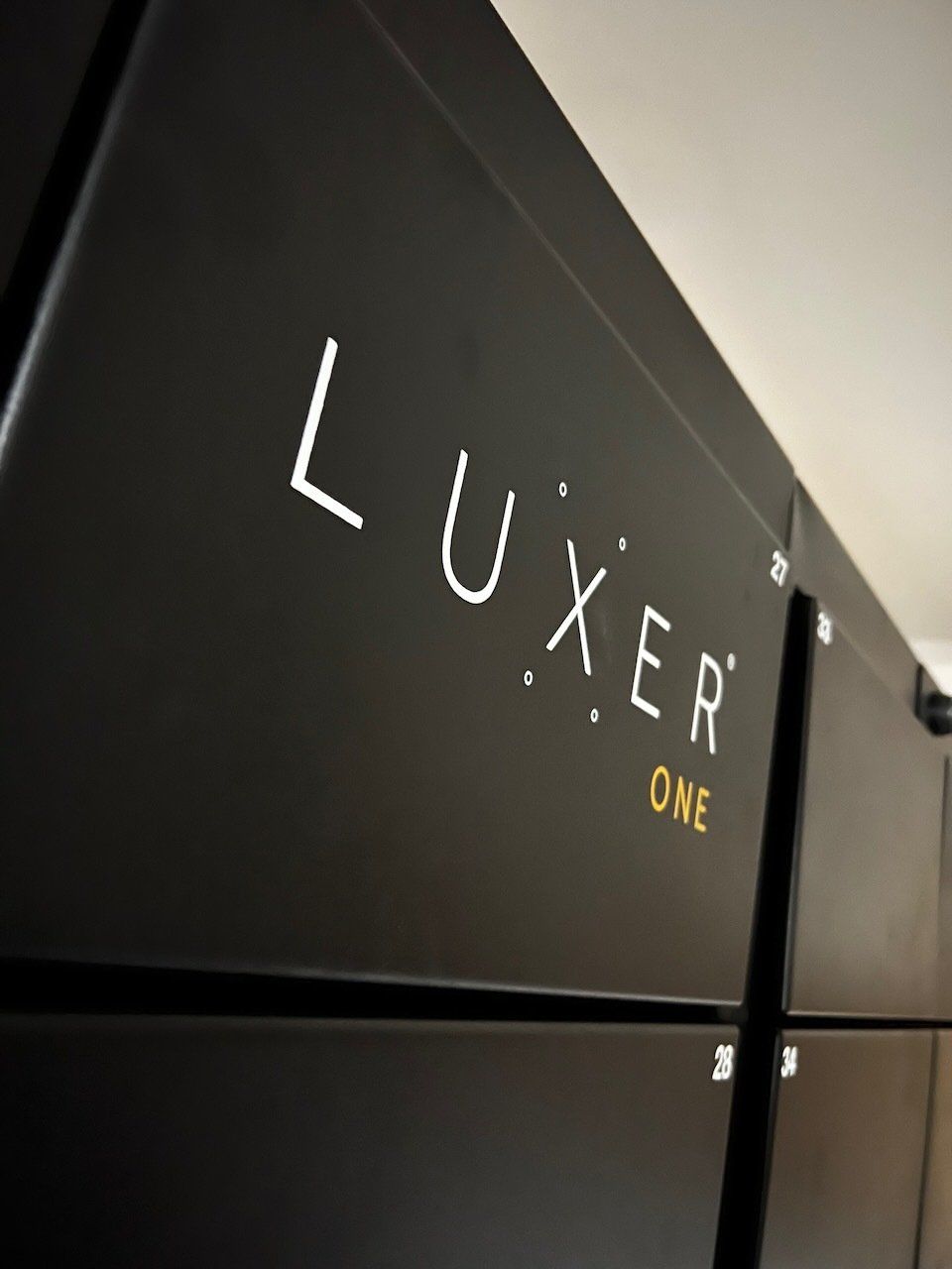 Black wall with the Luxier One logo in white and gold in a modern interior lobby.