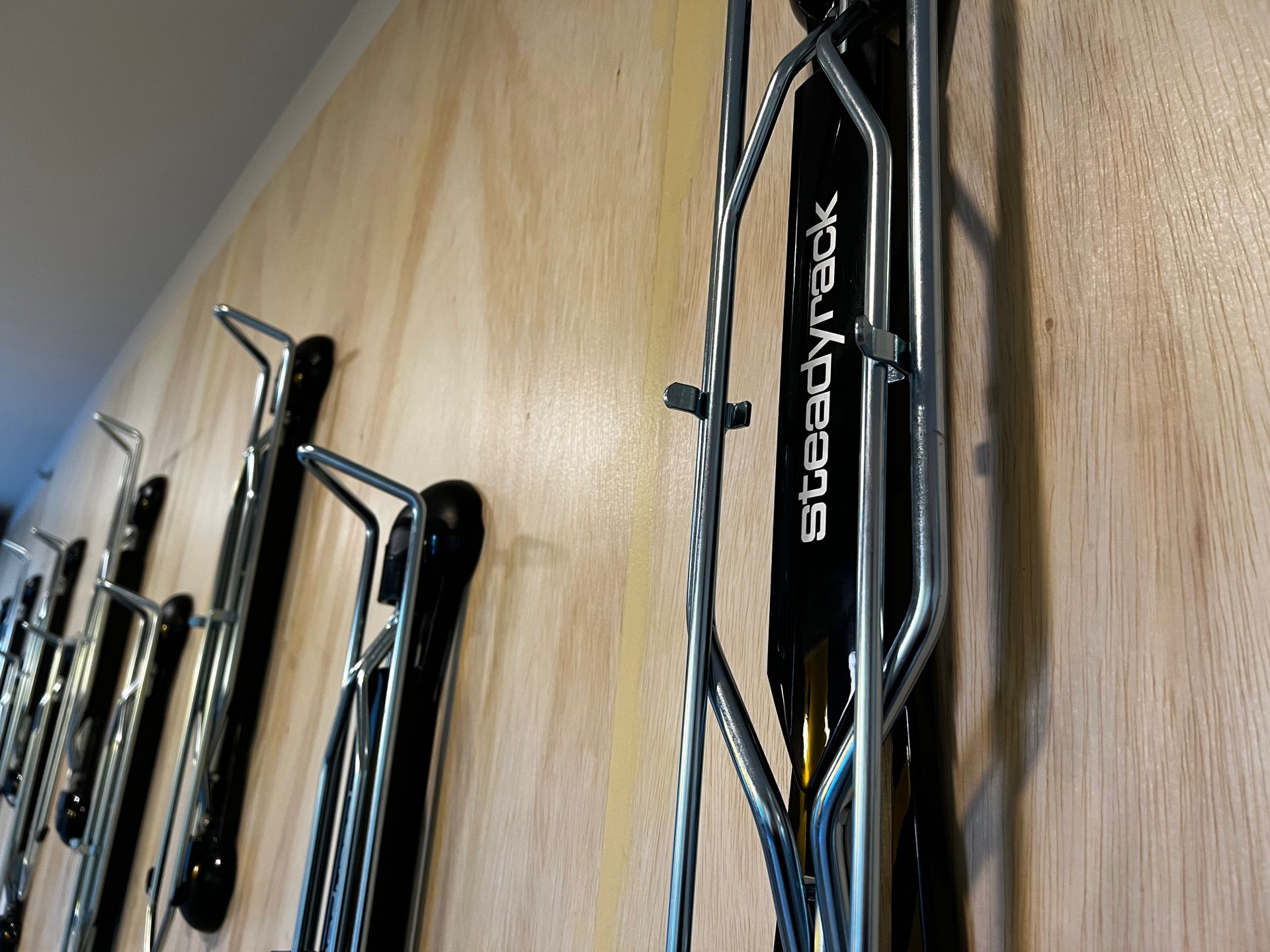 Row of black sports equipment mounted on a light wood wall, including a Speedplay item