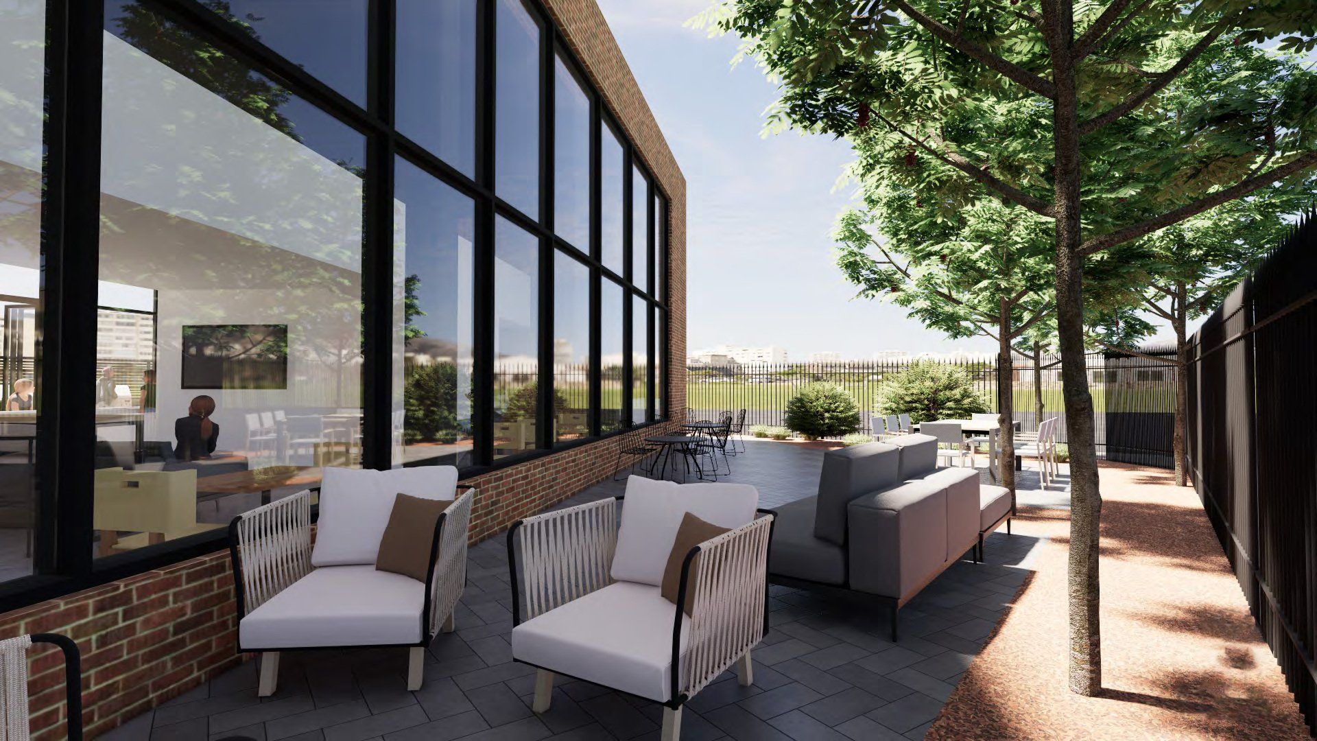 Patio seating beside a glass-walled building, with cushioned chairs and trees lining the walkway