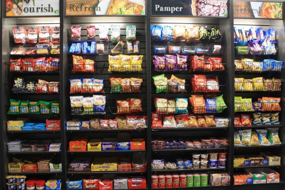 Convenience store snack aisle with rows of colorful packaged chips, candy, and pastries on shelves