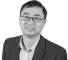 Man with glasses, wearing a suit jacket and dress shirt, smiling for the camera.
