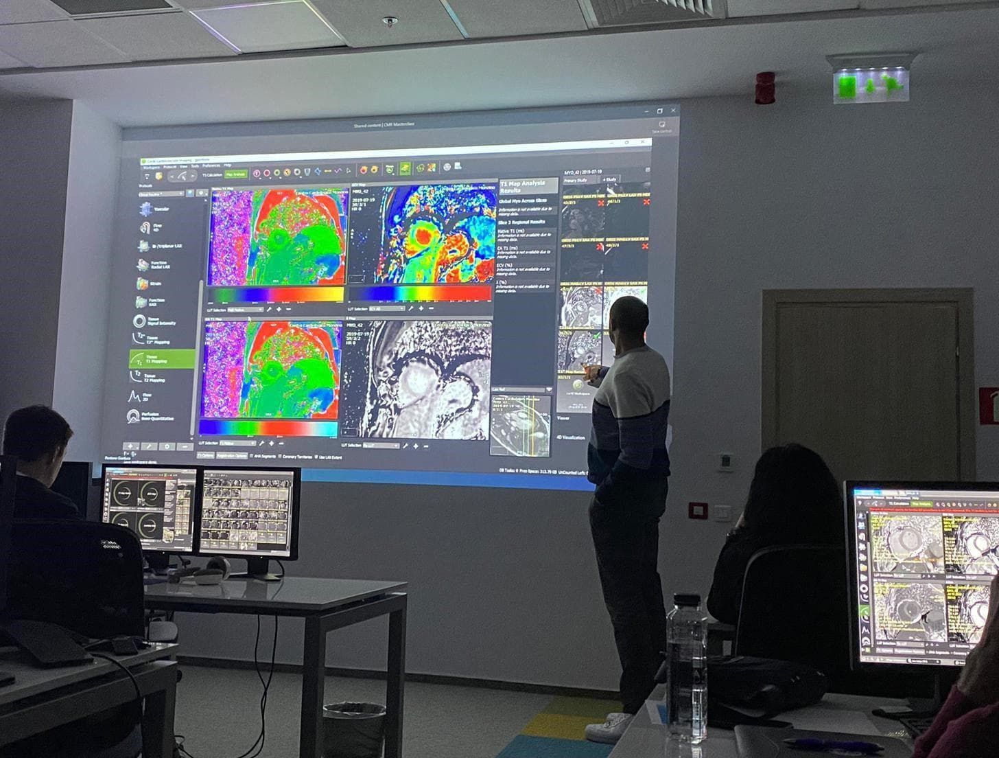 A man points to a projection screen displaying medical imaging software. Students watch, with computers on desks.