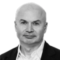 Bald man in a black jacket and white shirt, looking forward with a neutral expression.