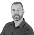 Man with a beard and short hair wearing a dark button-down shirt, looking directly at the viewer.