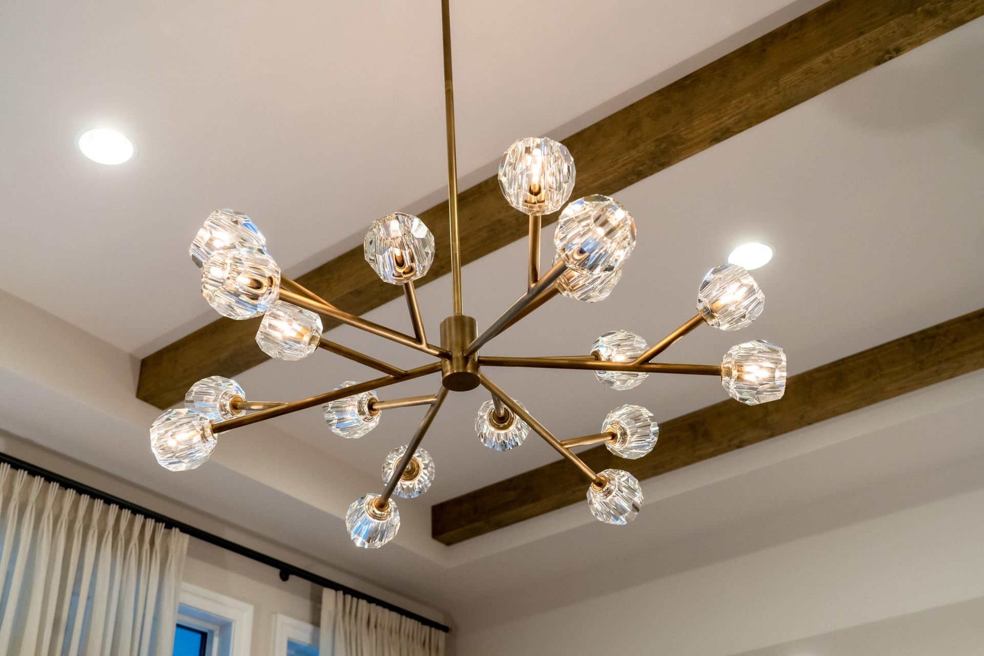 Gold chandelier with crystal ball lights hangs from a white ceiling with wood beams.