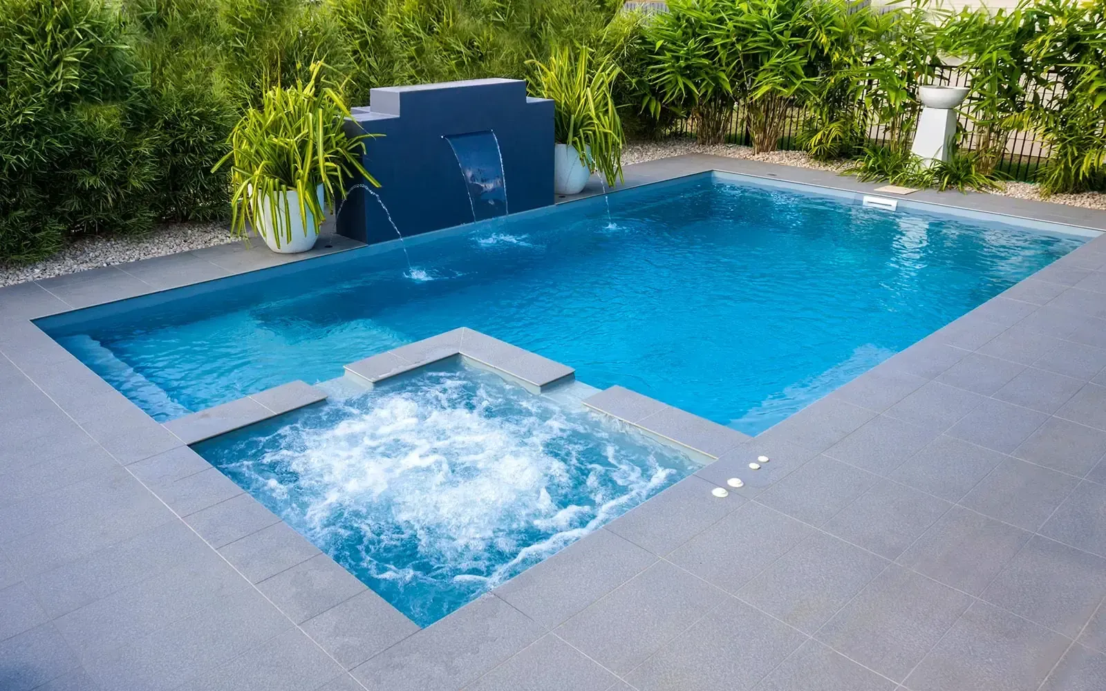 Blue backyard pool with waterfall feature and connected spa.