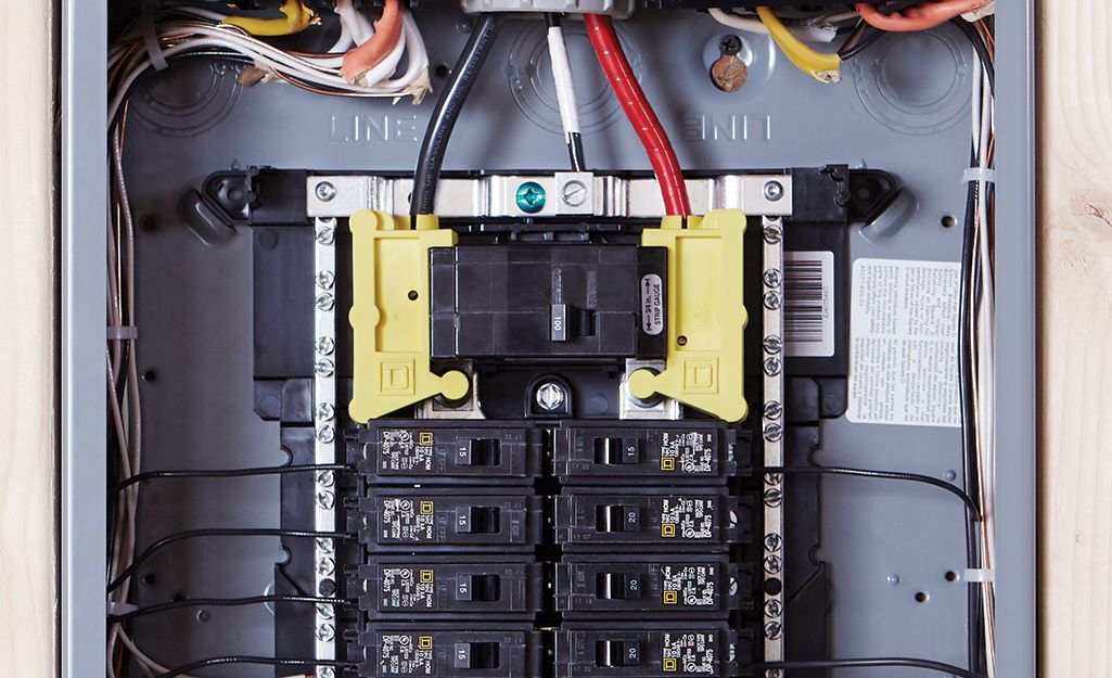 Electrical panel with black circuit breakers and yellow bars. Red, white, and black wires are visible.