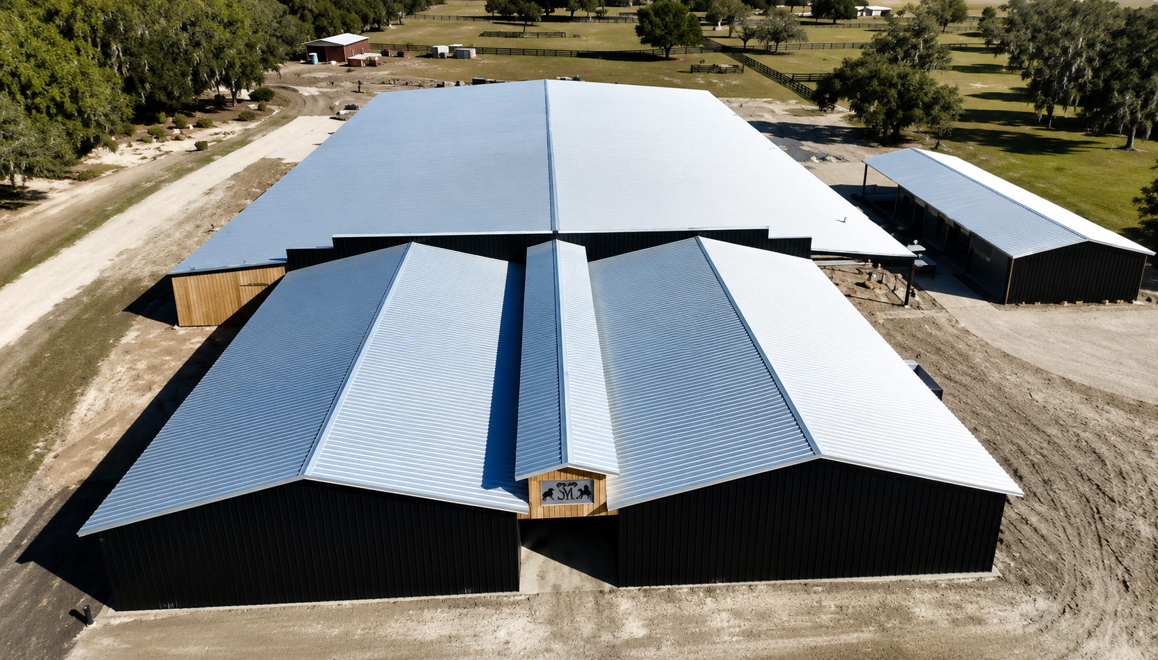 Aerial view of a large barn with blue and black metal roofs in a rural landscape