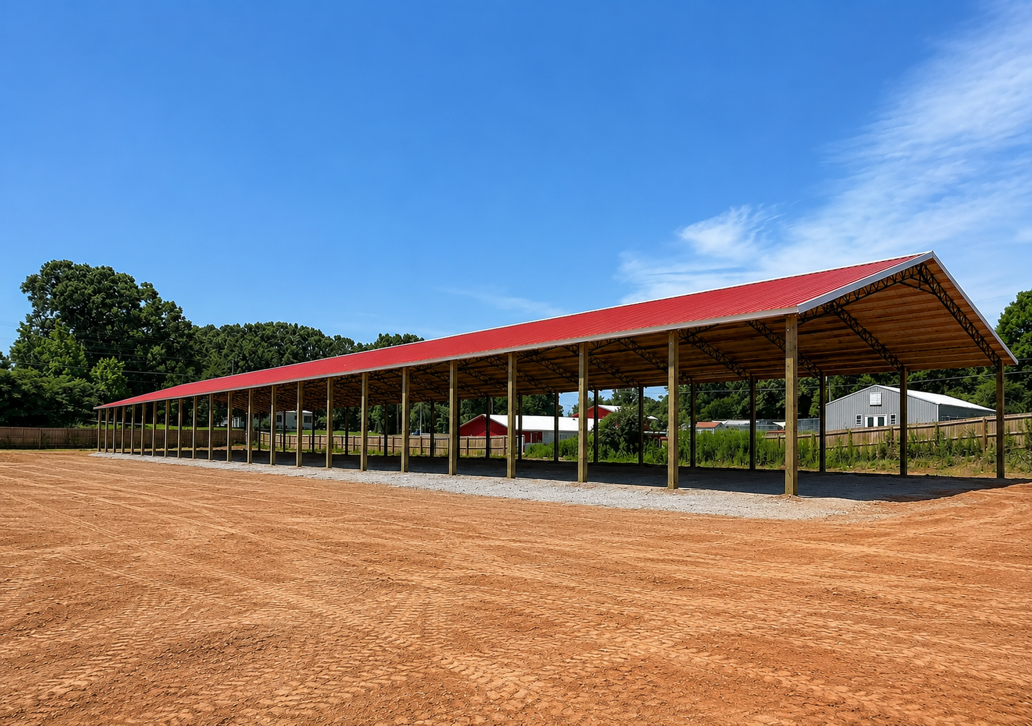 Wooden structure with a metal roof in a clearing, surrounded by trees and vegetation under a blue sky.