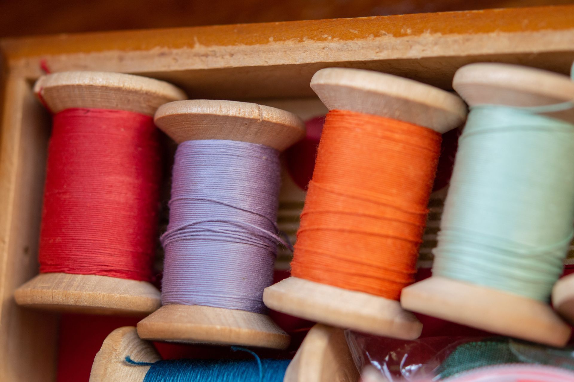 A wooden box filled with spools of thread of different colors.