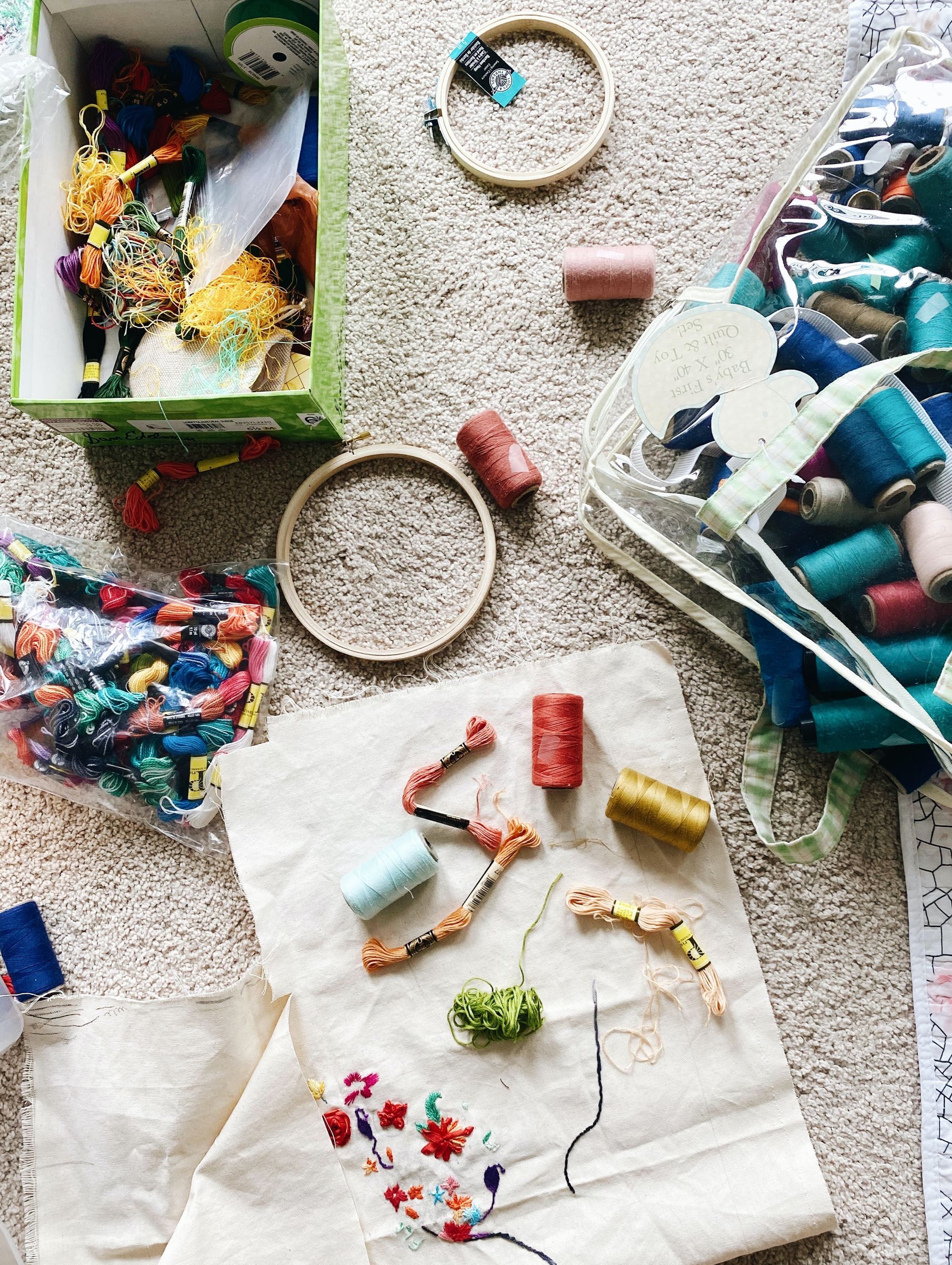 A bunch of embroidery supplies are sitting on the floor.