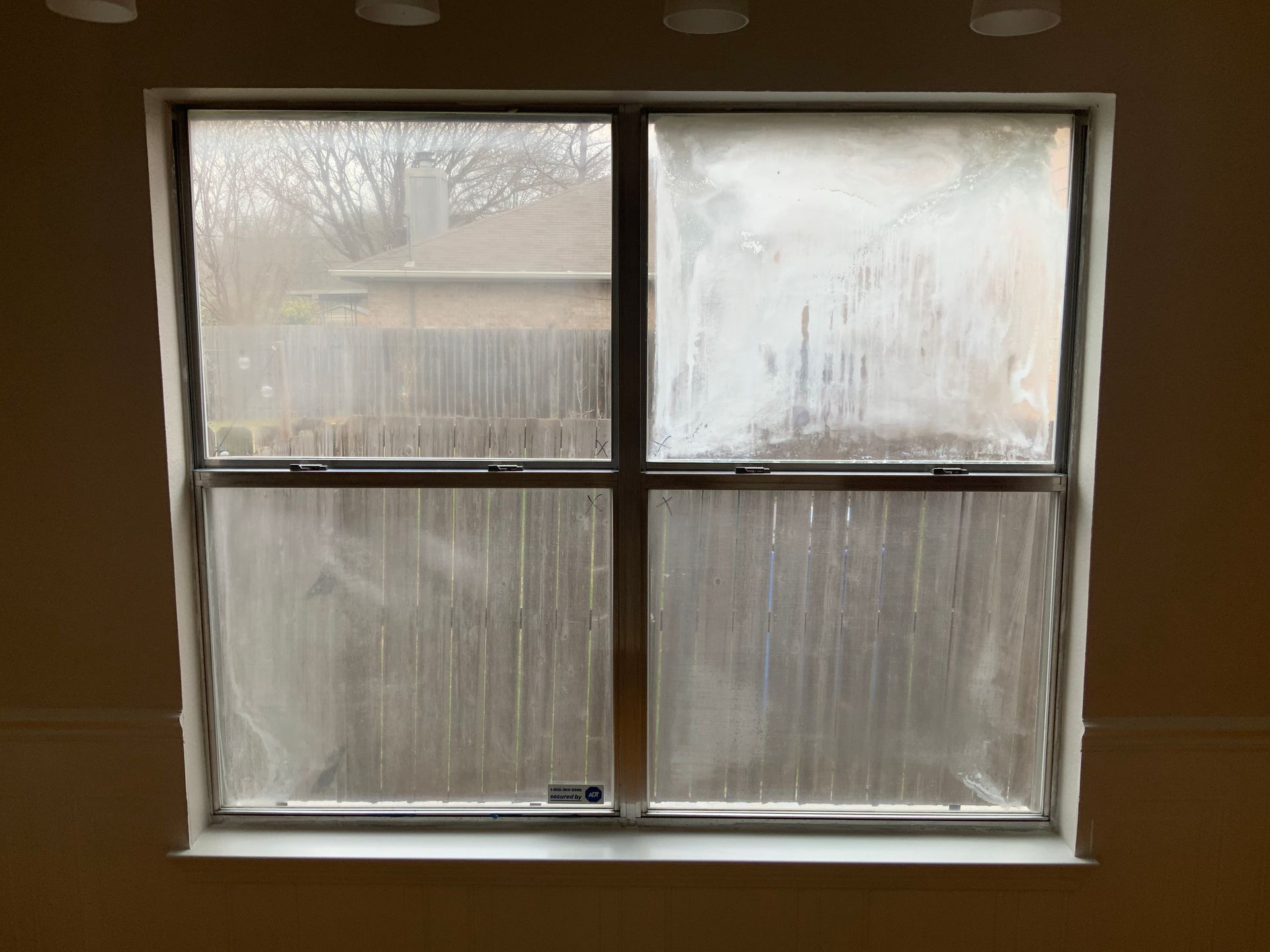 A dirty window in a room with a fence in the background