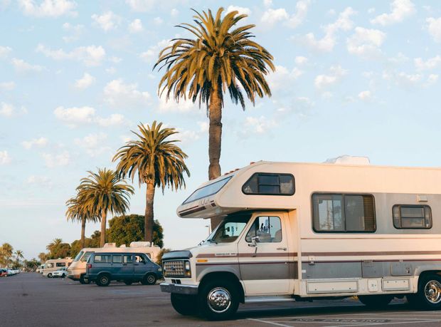A rv is parked in a parking lot with palm trees in the background.