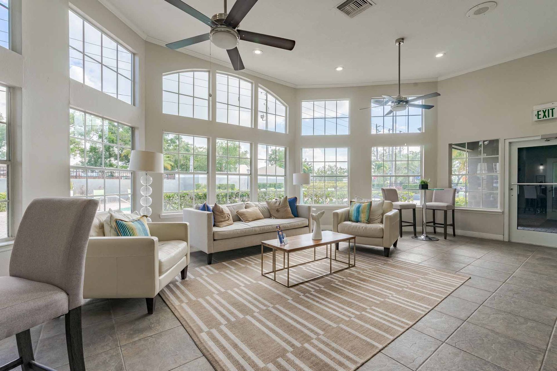Spacious resident clubhouse lounge area with large windows, cream-colored furniture, rug, two ceiling fans, and a bar area. Step inside our spacious 3-bedroom apartments in Clearwater, FL—schedule a visit.