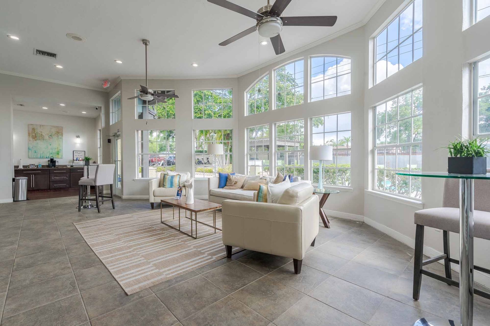 Resident clubhouse lounge area with large windows, white couches, rug, bar stools, and a small table. Tour our thoughtfully designed Apartments for Rent in Clearwater, FL at your convenience.