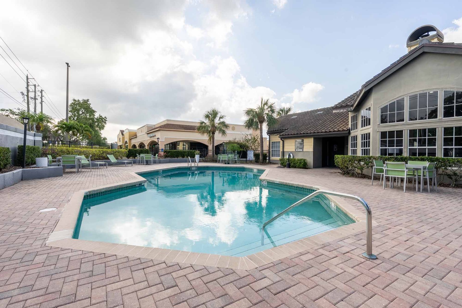 Pool with a building in the background, surrounded by brick patio and lounge chairs, under a cloudy sky. Come experience our welcoming Clearwater, FL apartments in person.
