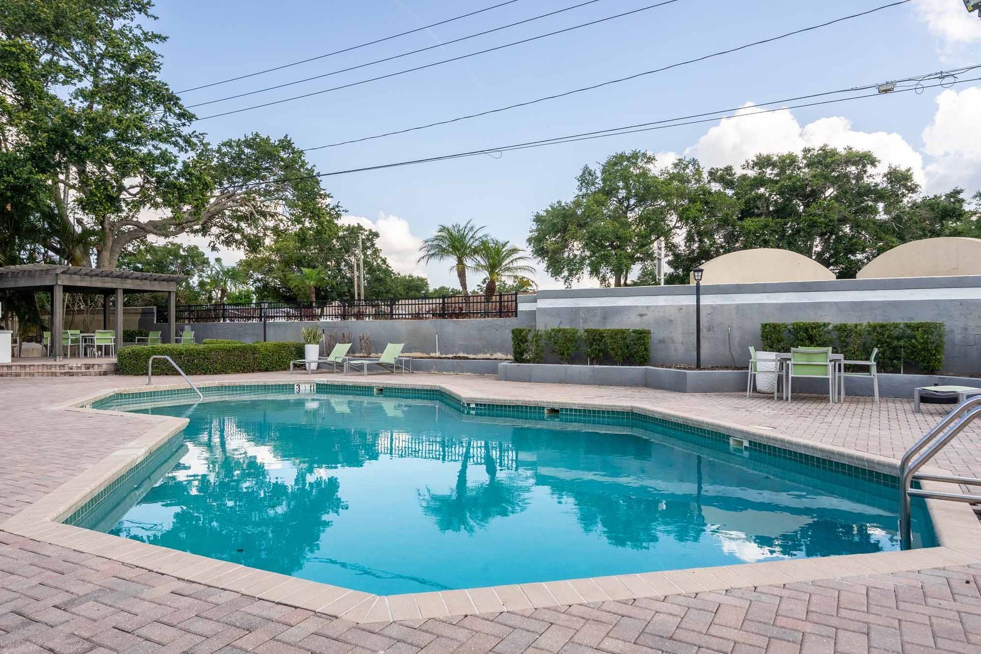 Swimming pool surrounded by brick with lounge chairs. Trees and sky overhead. Plan your tour and explore our comfortable Clearwater, FL apts.