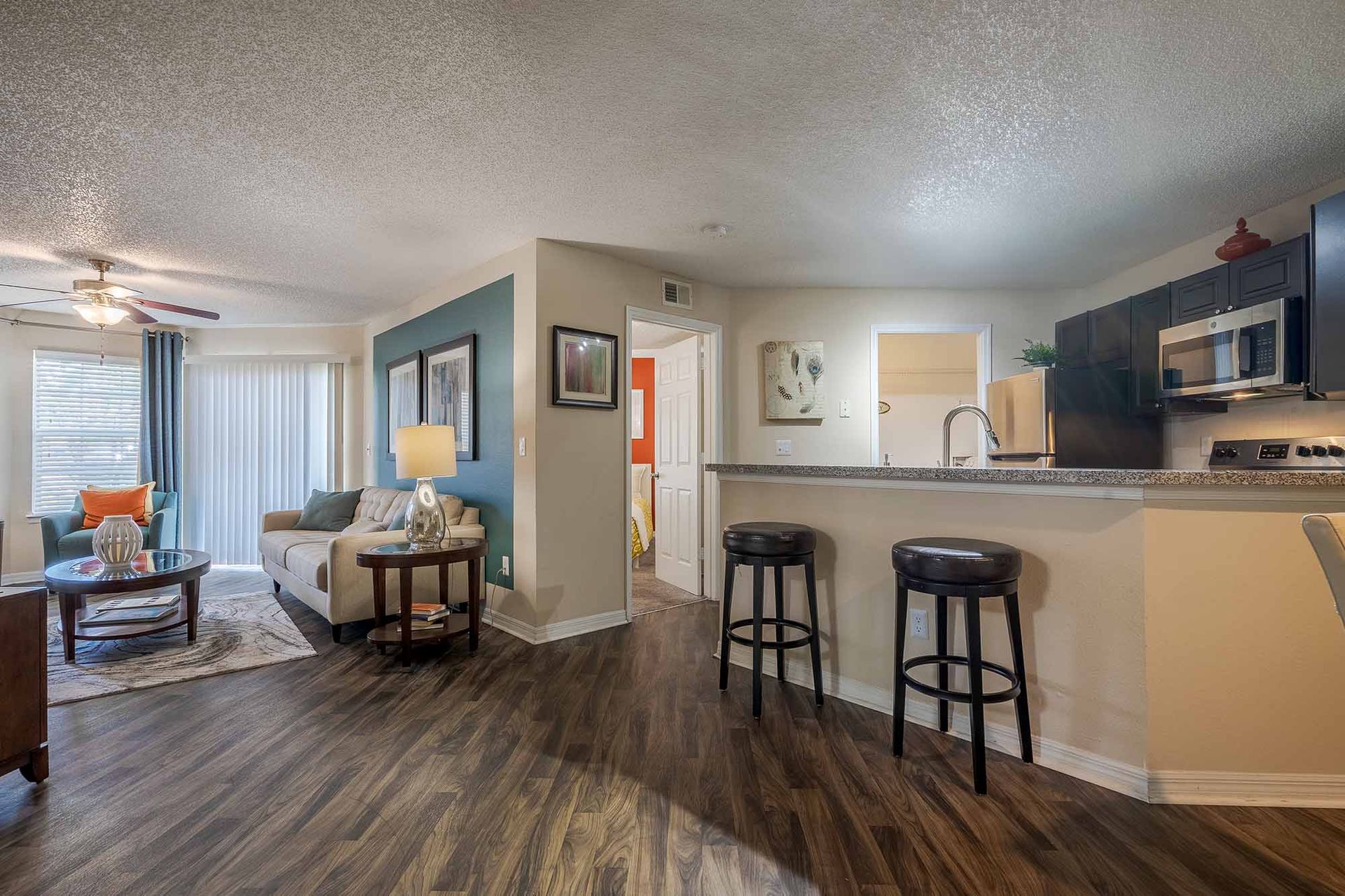 Open-concept apartment interior: living room, kitchen with breakfast bar, dark cabinets, seating, and wooden floors. Experience our Apartments in Clearwater, FL up close—schedule your visit.