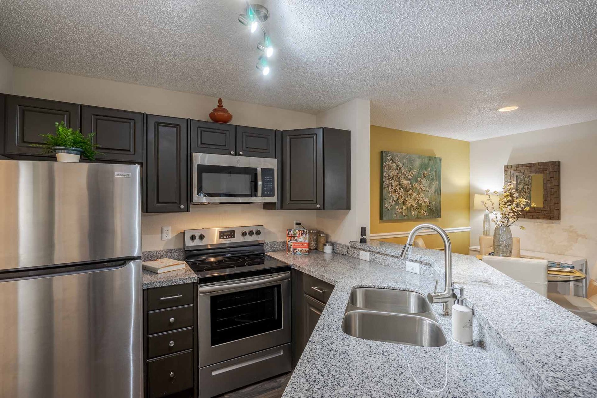 Modern kitchen with stainless steel appliances, gray cabinets, granite countertops, and a view of the living room. Schedule a tour today and explore Apartments for Rent in Clearwater, FL firsthand.