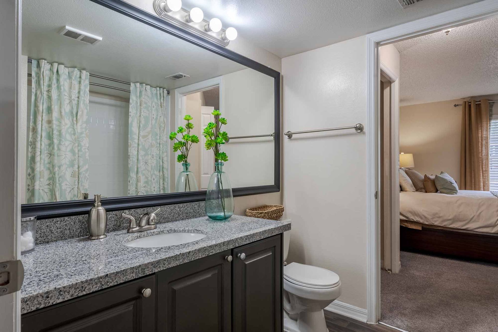 Bathroom with dark cabinets, granite countertop, large mirror, and open doorway to bedroom. Take a closer look at our inviting Apts in Clearwater, FL—book a tour.