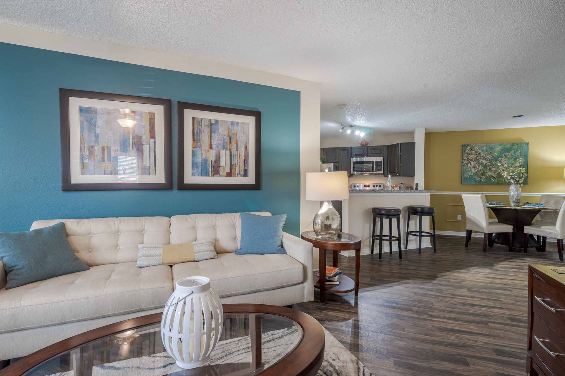 Living room with white sofa, blue accent wall, artwork, and view into the kitchen and dining area. See what sets our Clearwater, FL apts apart—plan your walkthrough.
