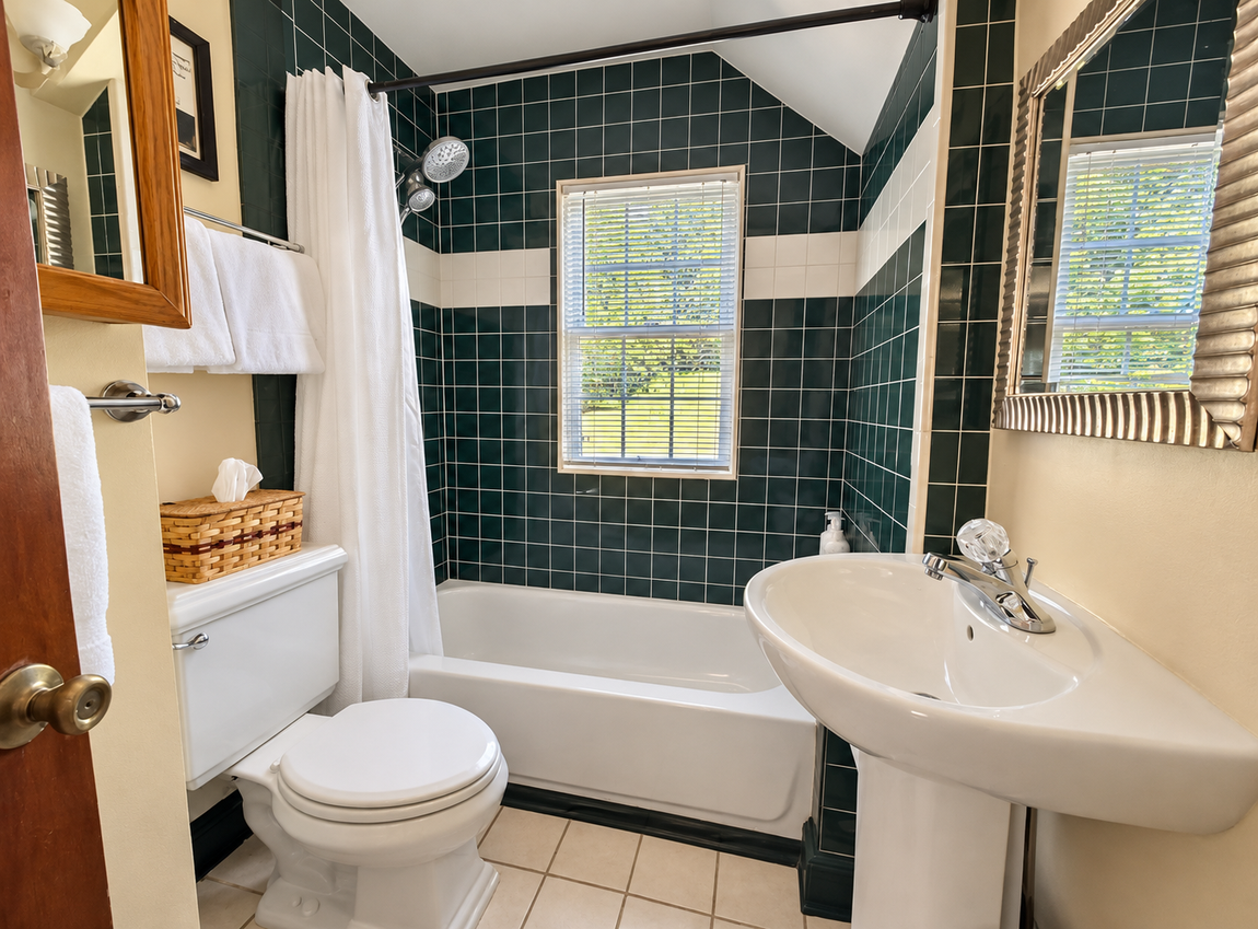 Red Fox Townhouse bathroom featuring a bathtub and shower with dark green tile, pedestal sink and natural window light.