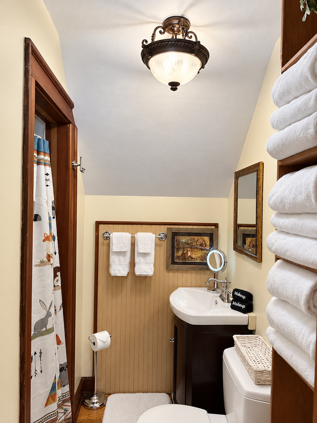 Bright upstairs bathroom at Red Fox Townhouse with shower, toilet, wooden door trim and neatly stacked towels.